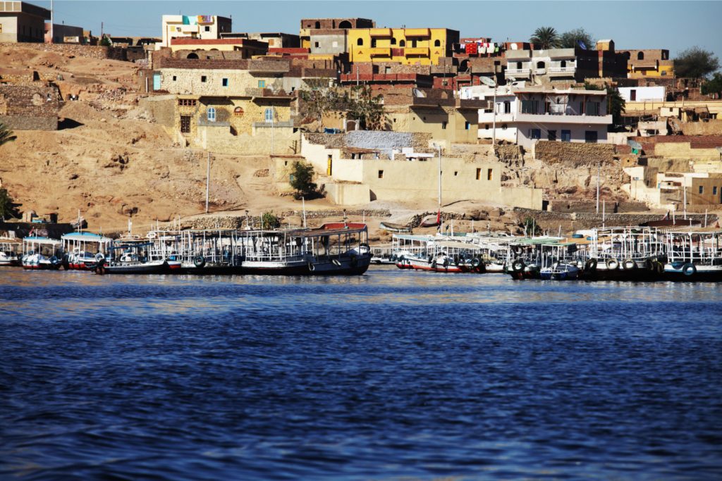 Brightly painted Nubian houses above the Nile near Aswan, with tourist boats moored below